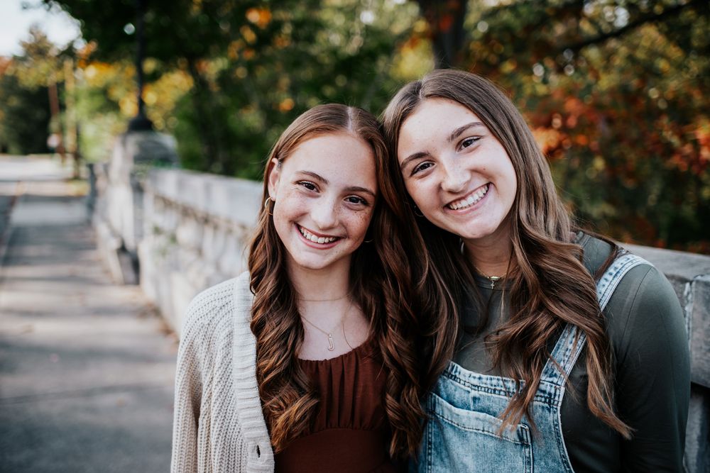 Two sisters smiling together on stone bridge during autumn.