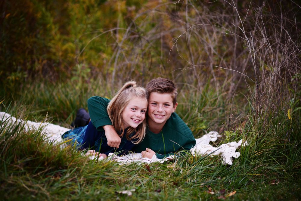 Siblings lying in grass during an outdoor photo session at sunset.