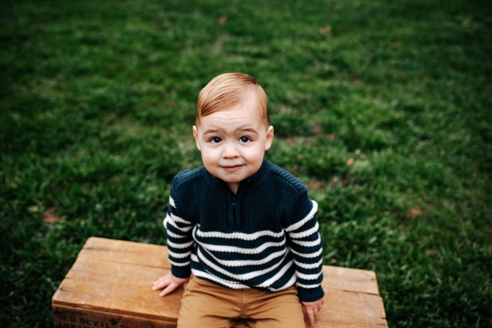 Child sitting on wooden bench wearing striped sweater outdoors.