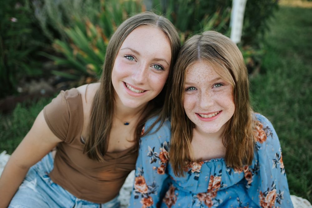 Siblings posing together outdoors in coordinating outfits against a natural green background.