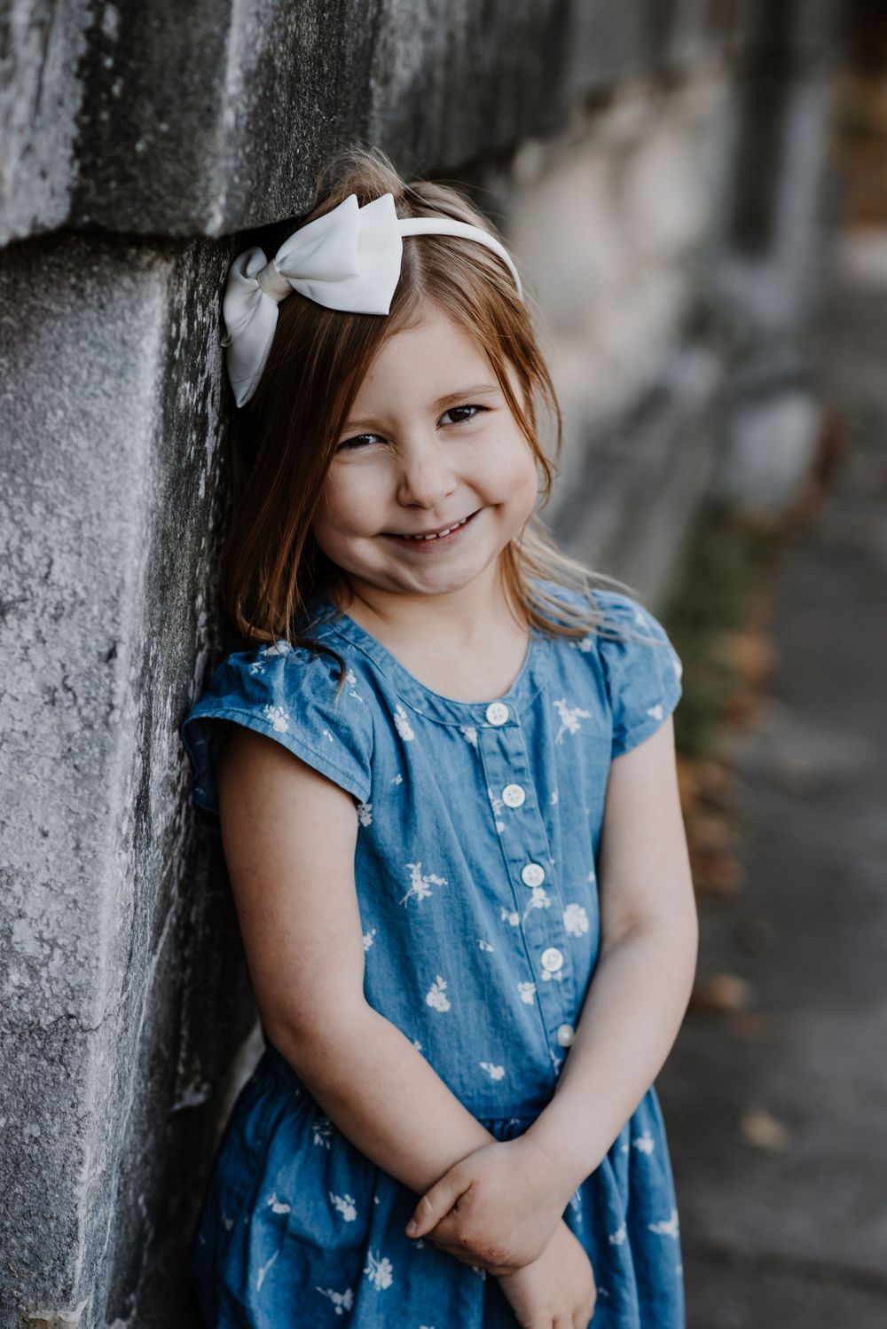 A sequence of portraits showing a child in a blue dress posing against a stone wall.