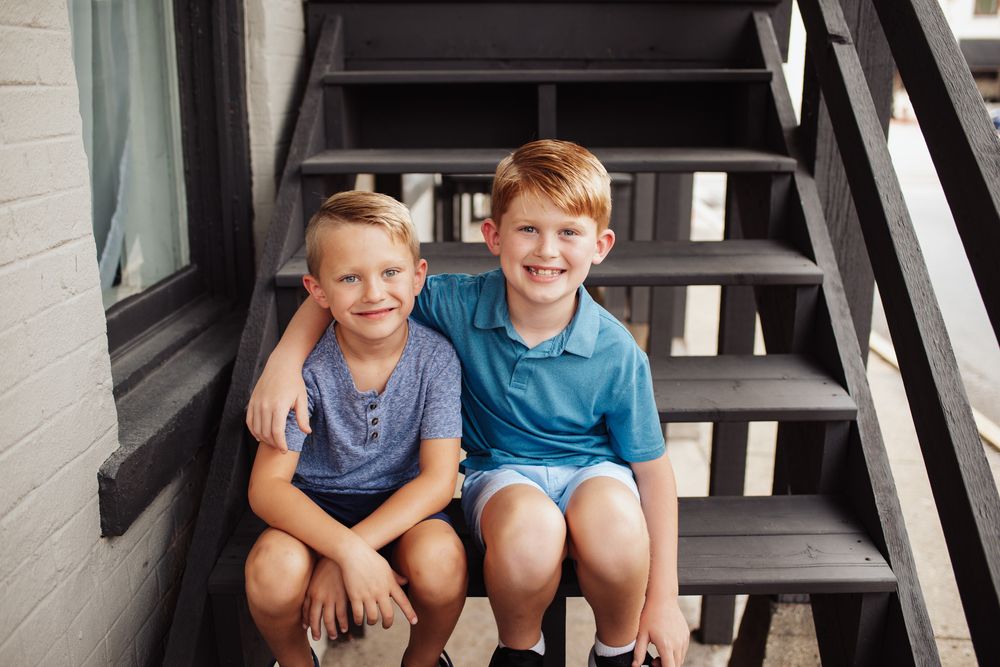Two young children sitting together on gray wooden stairs outside a building.