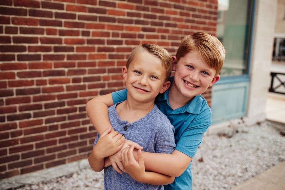 Two children hugging and laughing while sitting on steps near a brick wall.