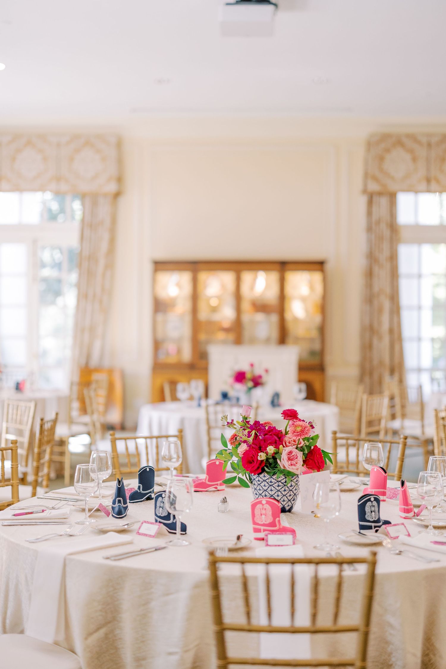 Empty wine glasses lined up at a banquet with red paper decorations hanging above them against a warm yellow background.