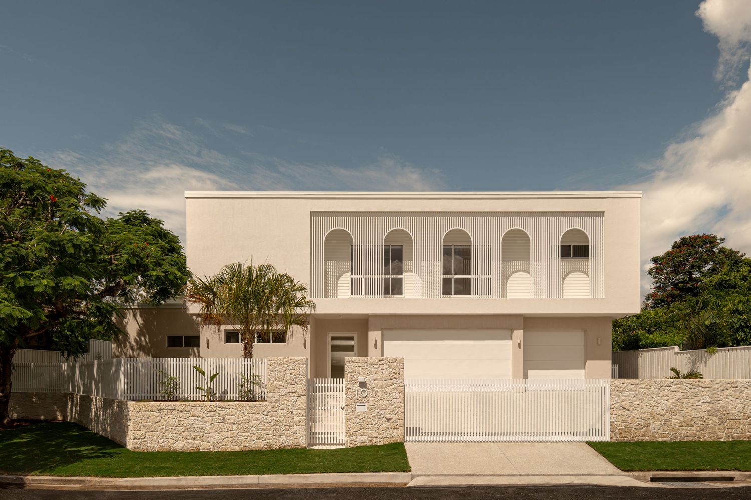 Modern white minimalist house with arched windows and stone facade features clean lines and landscaped grounds.