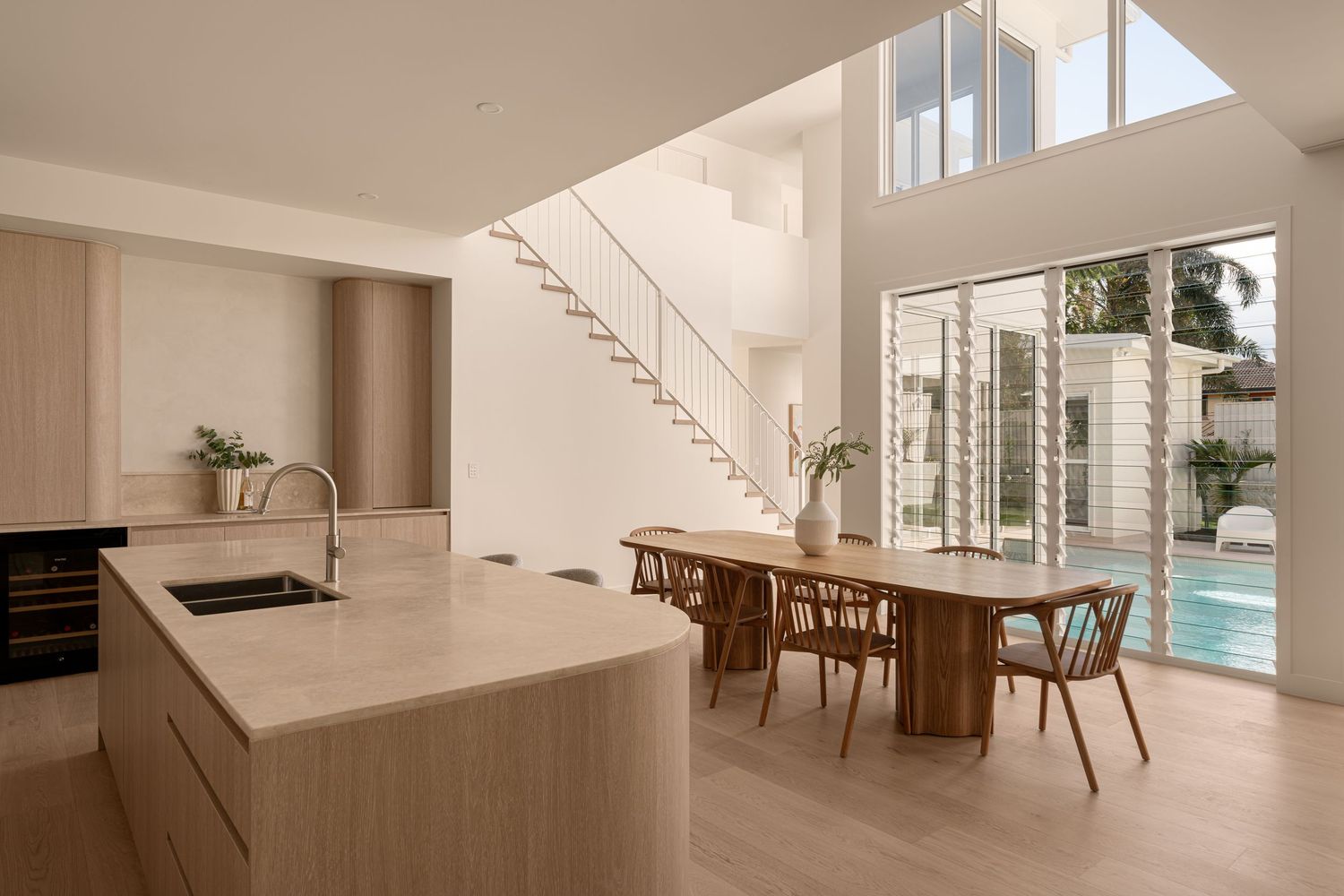 Modern open concept kitchen and dining area with light wood finishes, floating staircase and floor-to-ceiling windows.