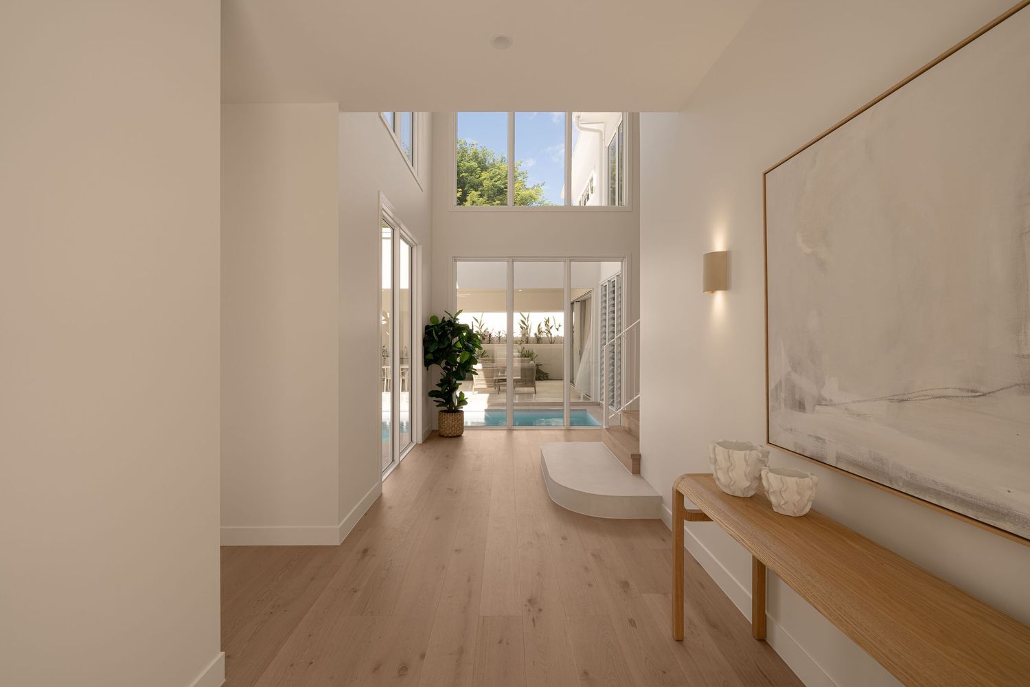 Modern minimalist hallway with white walls, wooden flooring and natural light streaming through windows.
