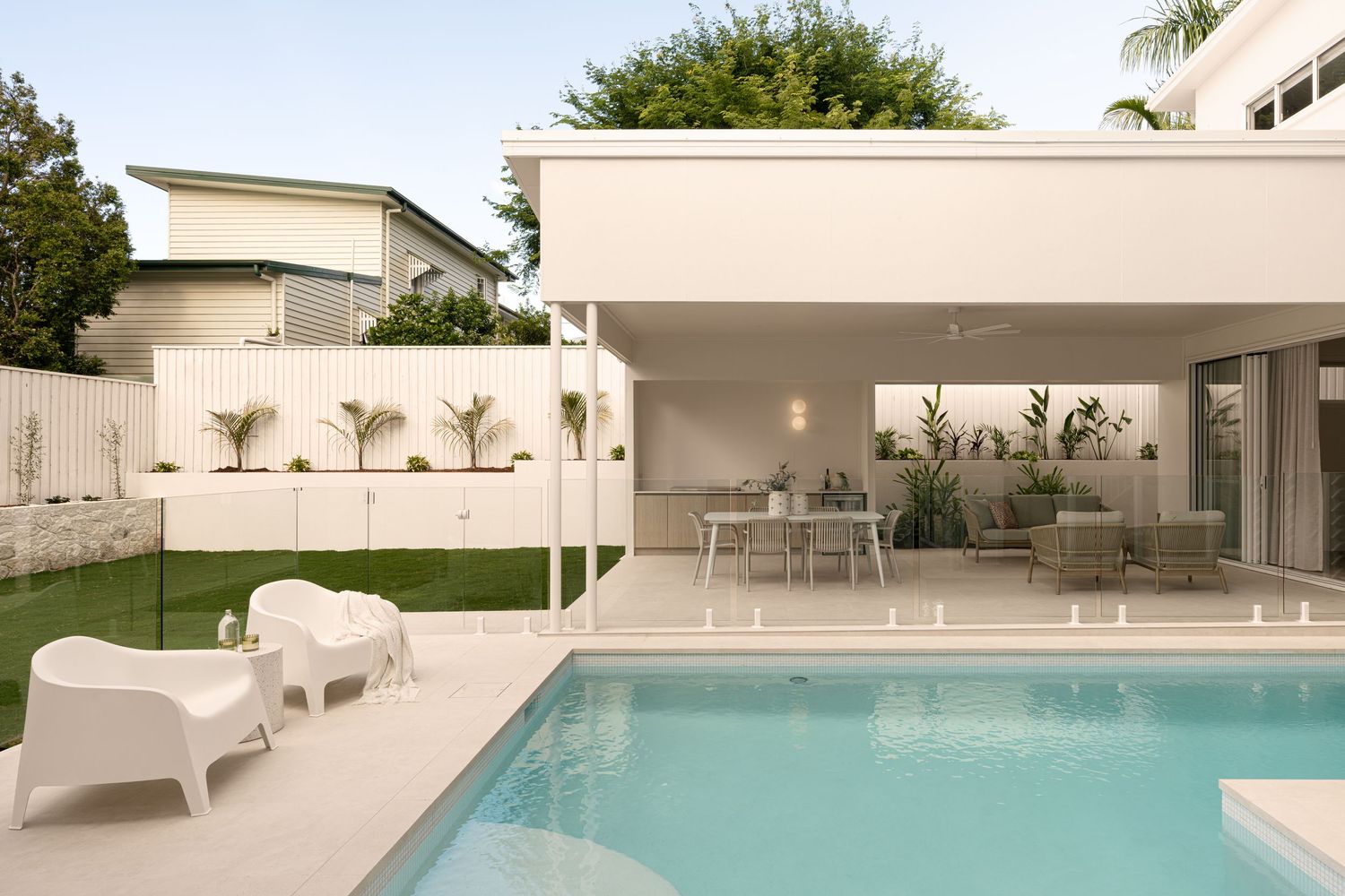 Modern luxury swimming pool with white lounge chairs and palm trees surrounding a sleek outdoor patio area.