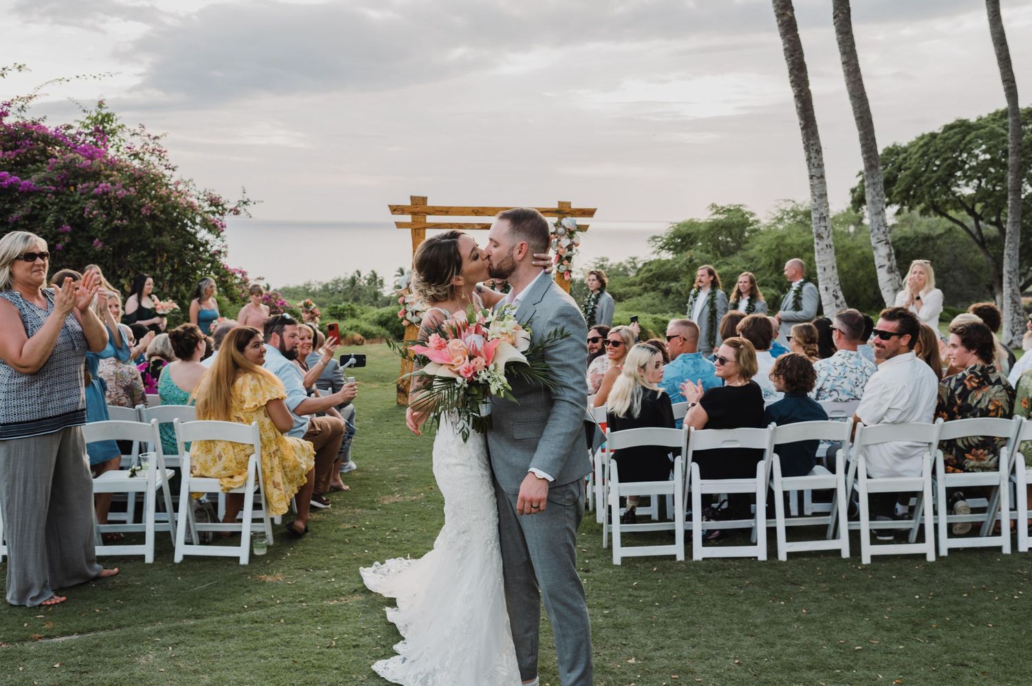 Outdoor wedding ceremony setup with white chairs and tropical palm trees in the background.
