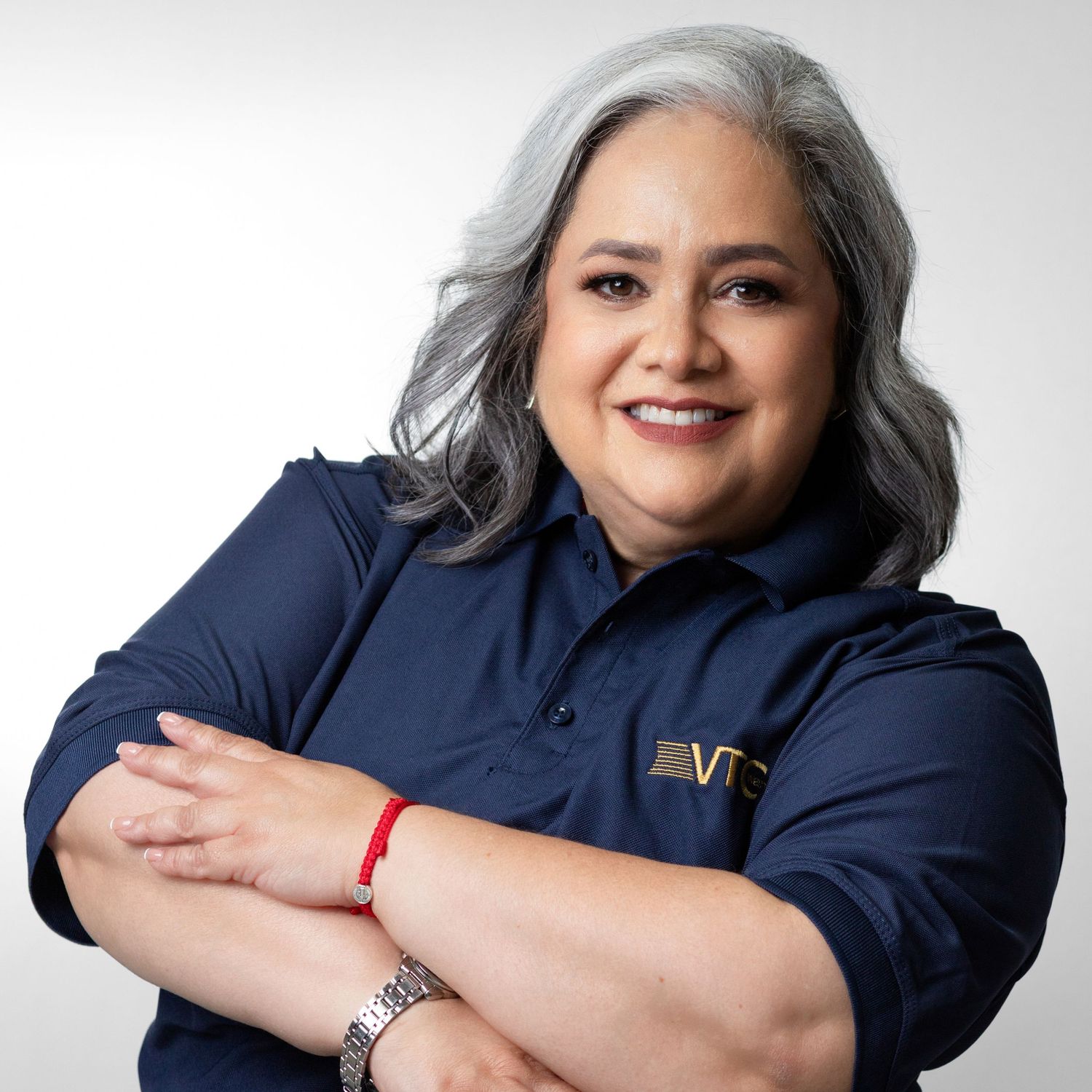 Professional portrait of someone in a navy blue polo shirt with silver hair and crossed arms against a light background.