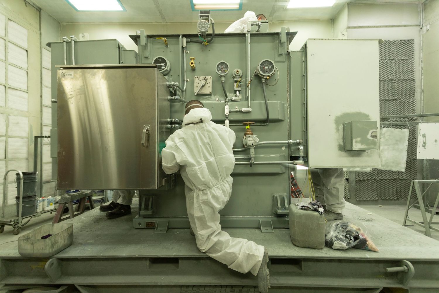 Clean room facility with workers in white protective suits operating manufacturing equipment.