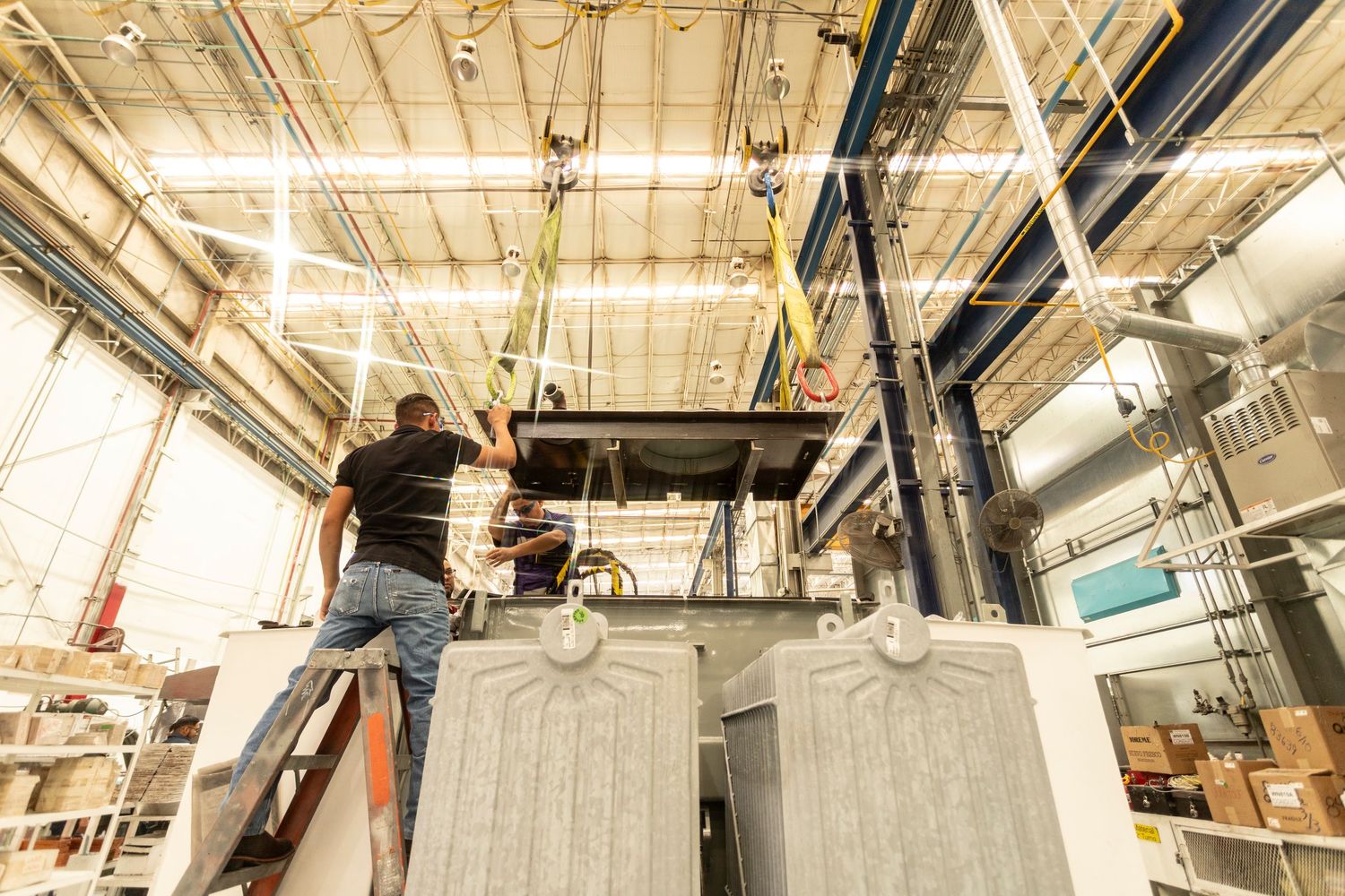 Workers install equipment on elevated platforms inside an industrial warehouse facility.