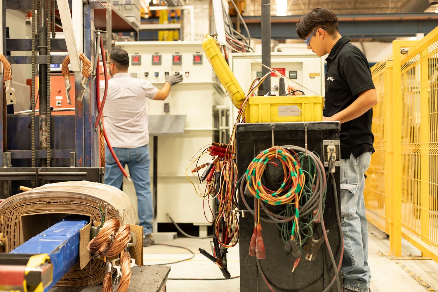 Industrial workers perform maintenance on yellow machinery equipment in a factory setting.