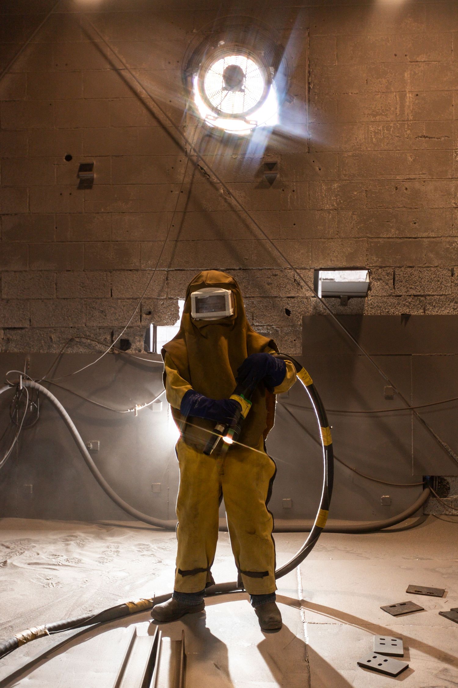 Worker in protective yellow suit sprays cleaning solution in industrial crawl space during maintenance work.