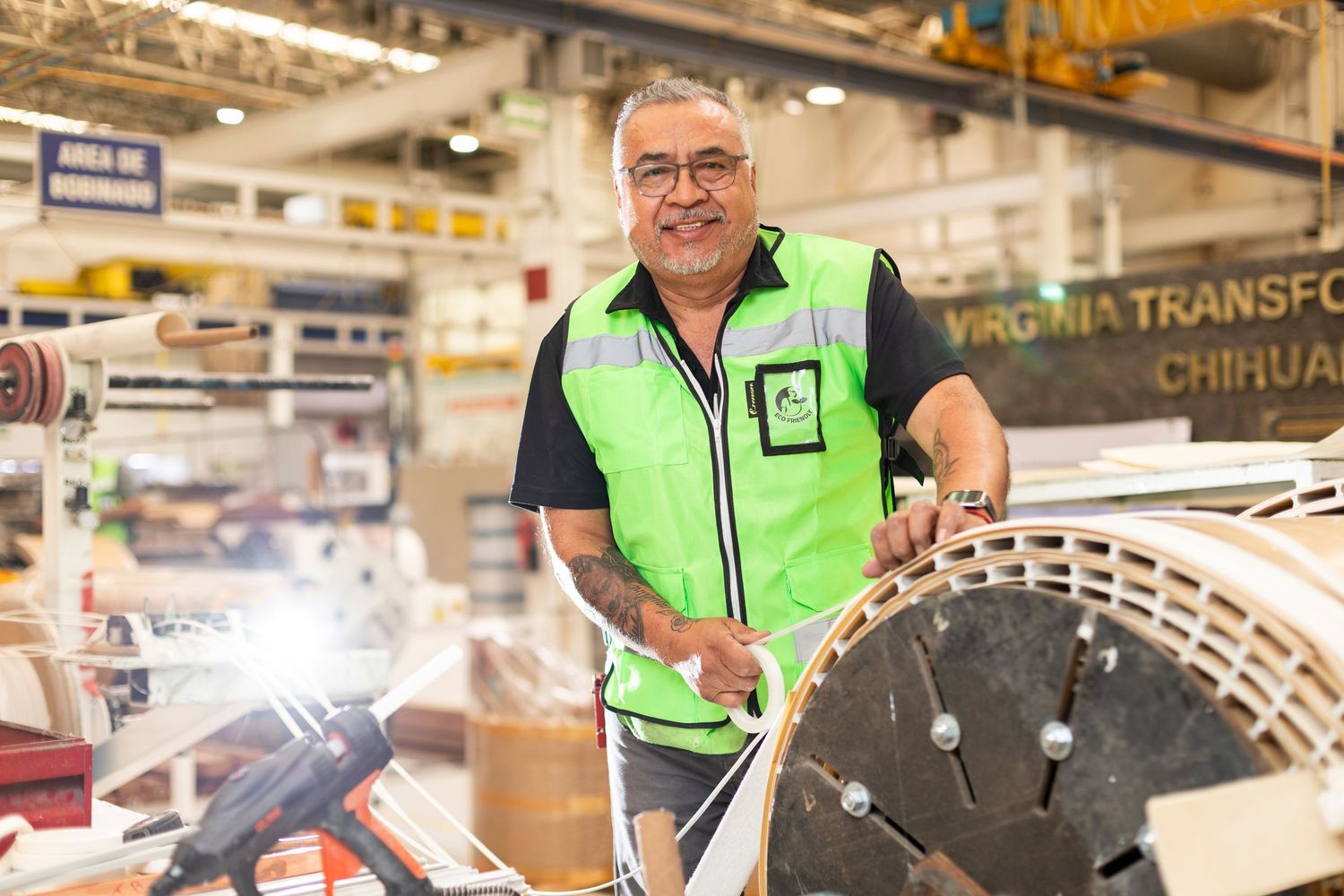 Workers in high visibility vests inspect and maintain equipment in a large industrial warehouse facility.