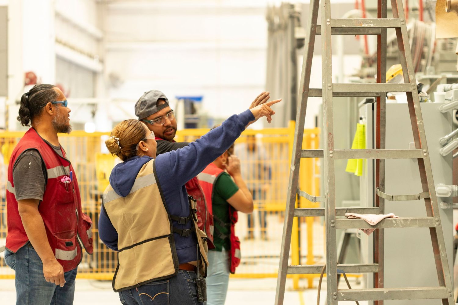 Workers in safety vests inspect and maintain industrial equipment in a manufacturing facility.