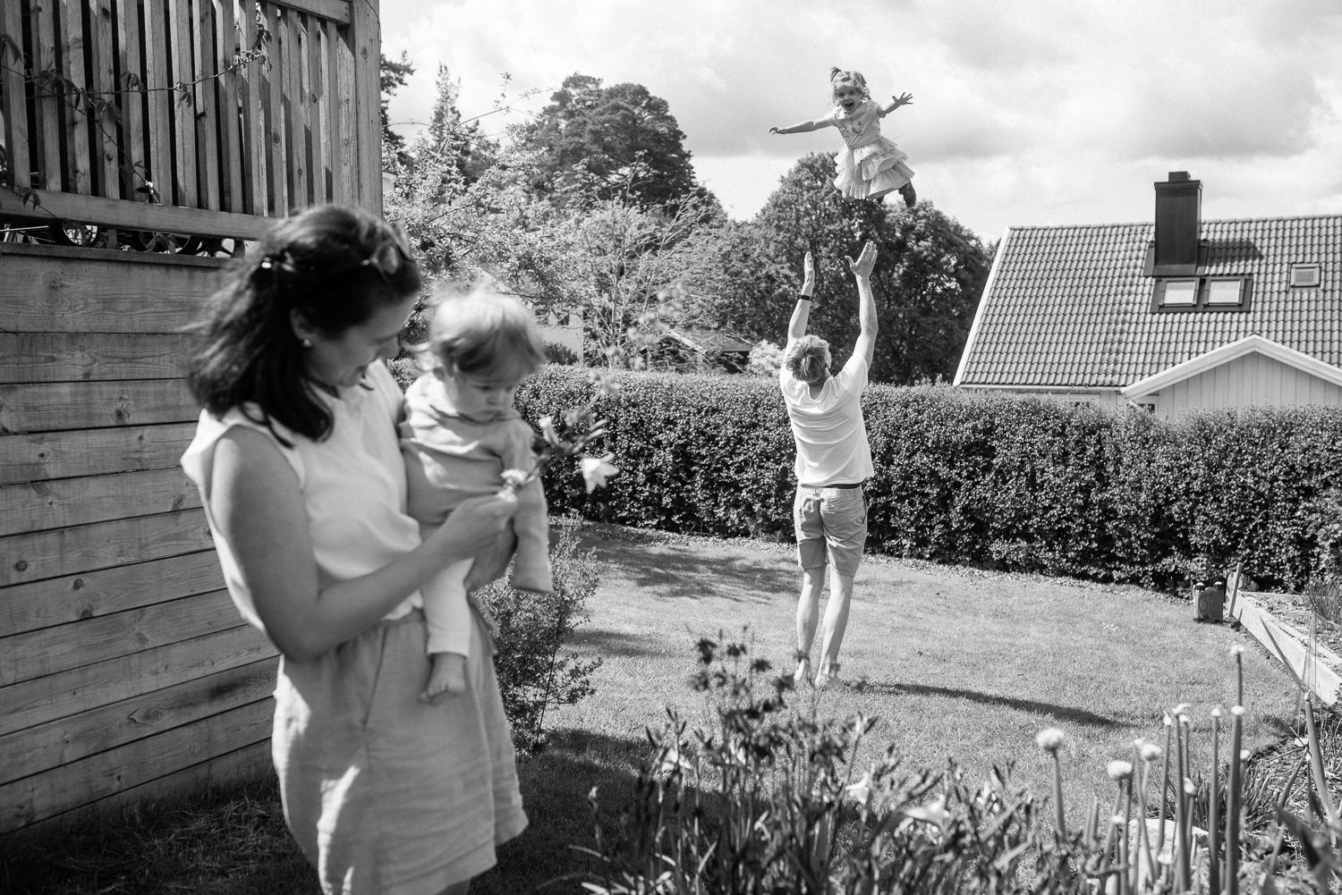 A joyful moment captured in a backyard garden as people play and lift a child up into the air on a sunny day.