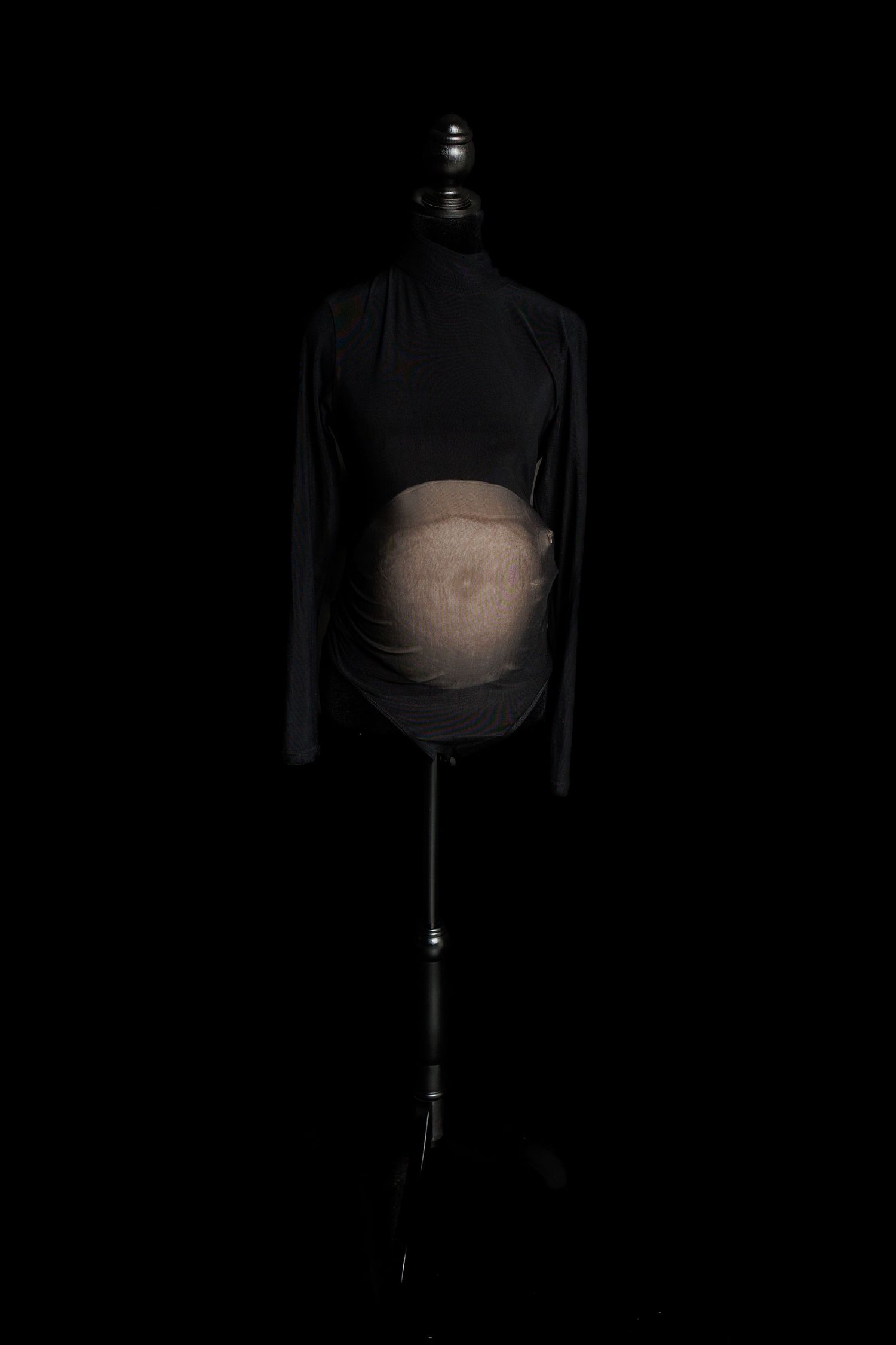 Black sheer long-sleeve maternity bodysuit with high neckline and fitted silhouette displayed on a dress form.