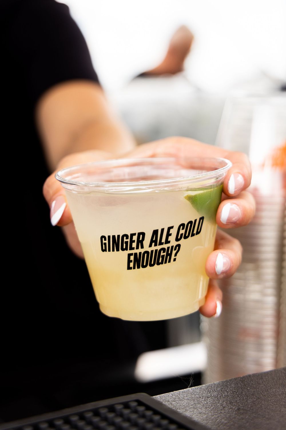 Person holding a plastic cup of ginger ale with lime garnish and text reading Ginger Ale Cold Enough?.