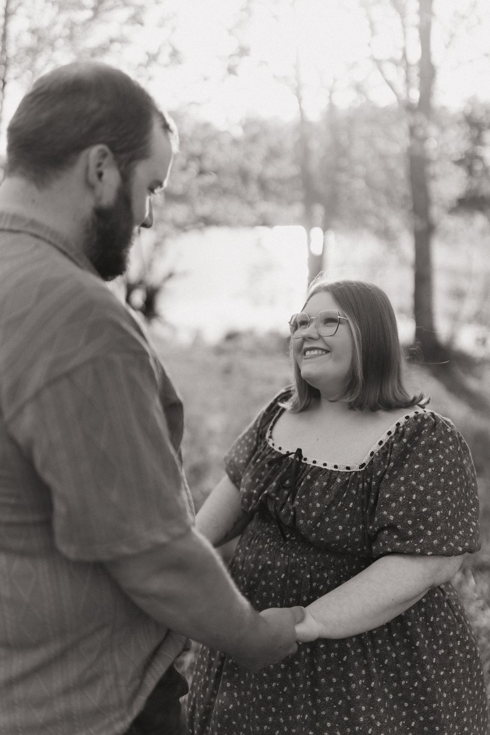 A couple shares a tender moment outdoors in black and white, with the woman wearing a polka dot dress smiling joyfully.