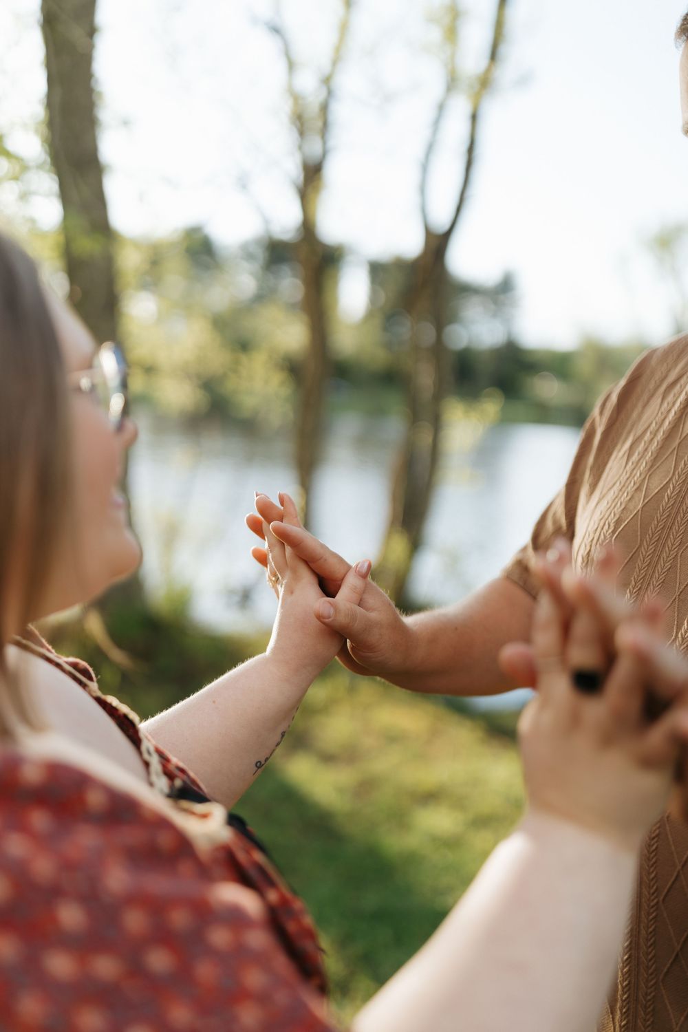 Close-up of hands clasped together tenderly against a sunlit lakeside background.