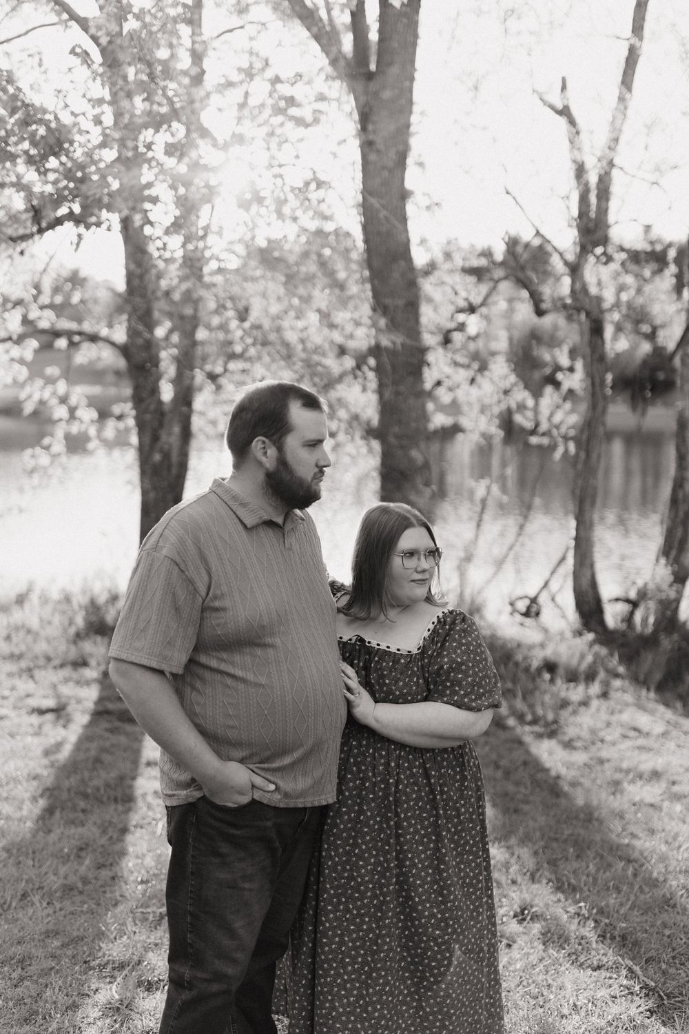A romantic couple poses together in a wooded area for black and white engagement photos.