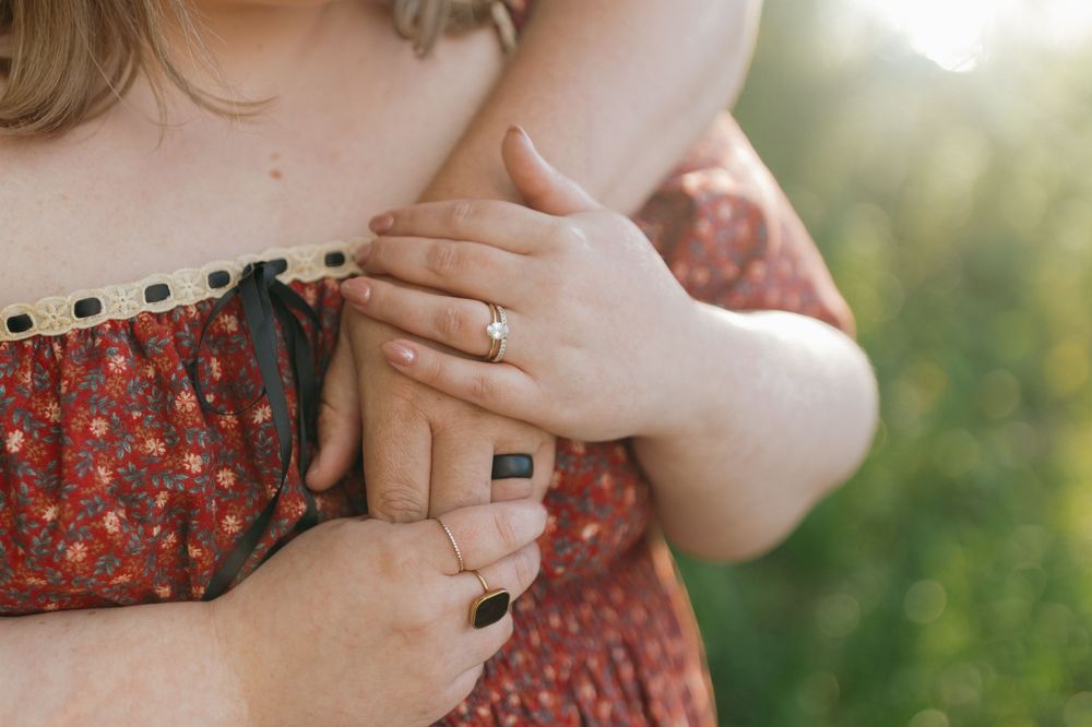 Close-up of hands wearing a ring against a red floral dress with soft natural lighting in the background.