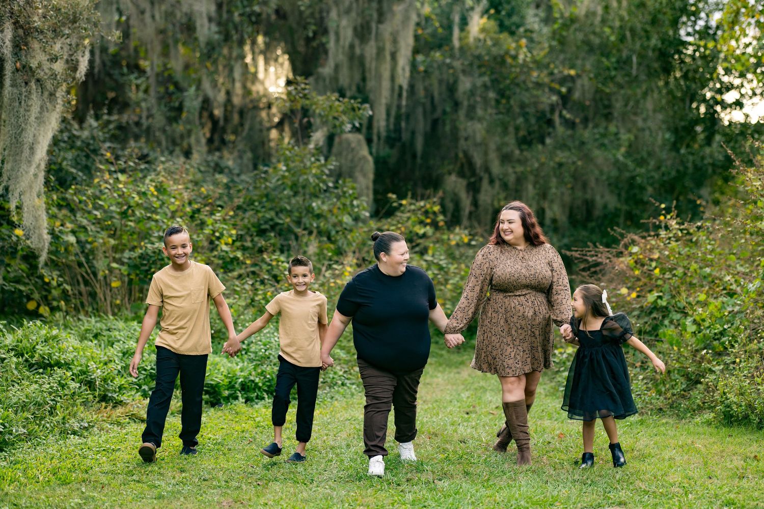 A group of people holding hands while walking together in a lush green outdoor setting with Spanish moss in the trees.