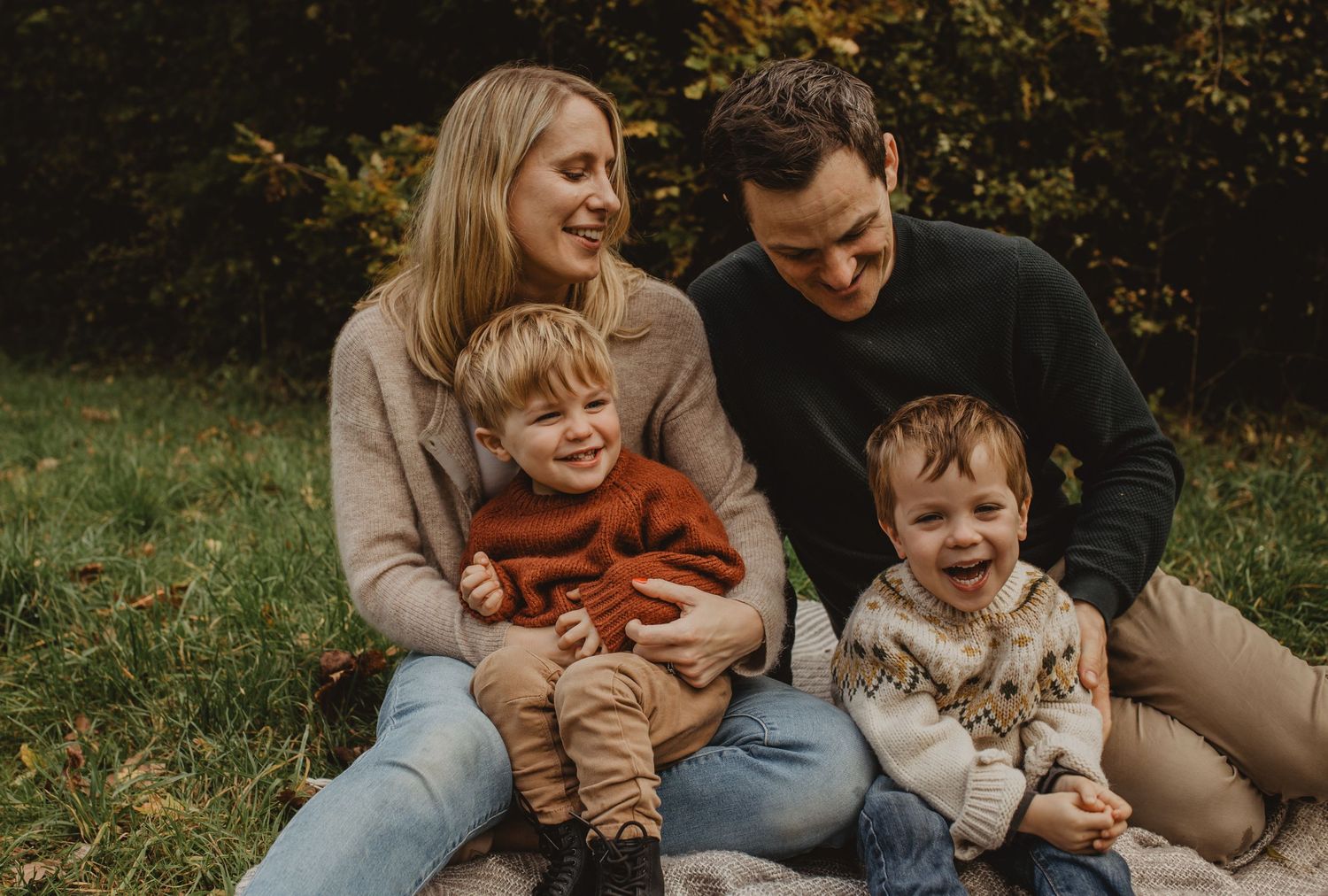 A family sits together on grass during an autumn day wearing cozy sweaters.