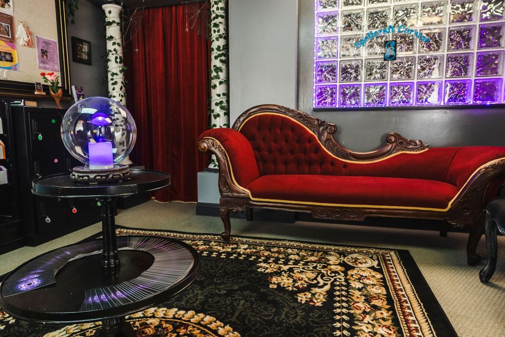A vintage red velvet fainting couch sits beside a plasma ball in a room with purple-lit glass block windows.