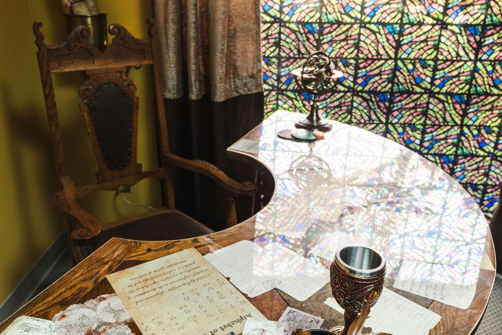 Vintage writing desk with handwritten papers, wine glass and stained glass window in background.