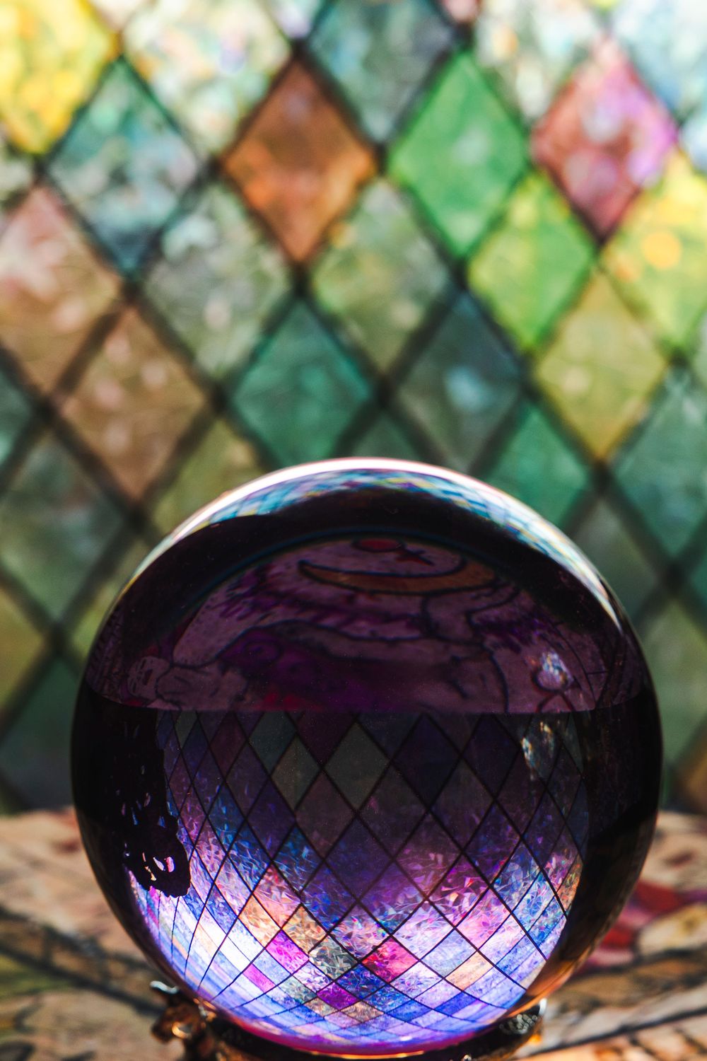 Crystal ball reflects colorful stained glass pattern creating magical rainbow effect against blurred background.