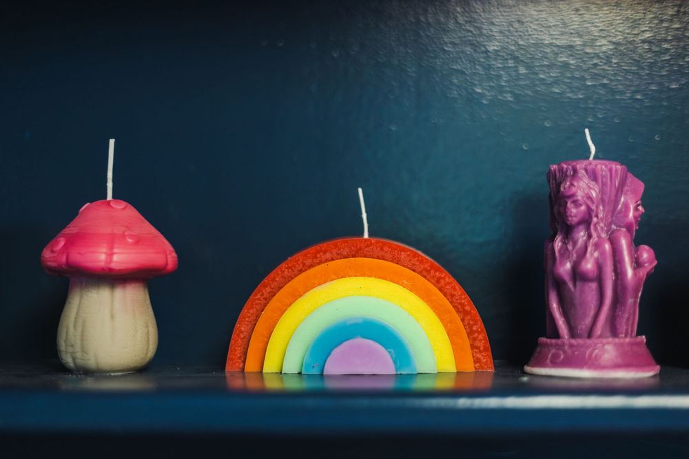 Colorful decorative candles featuring a mushroom, rainbow, and unicorn figure arranged on dark blue shelf.