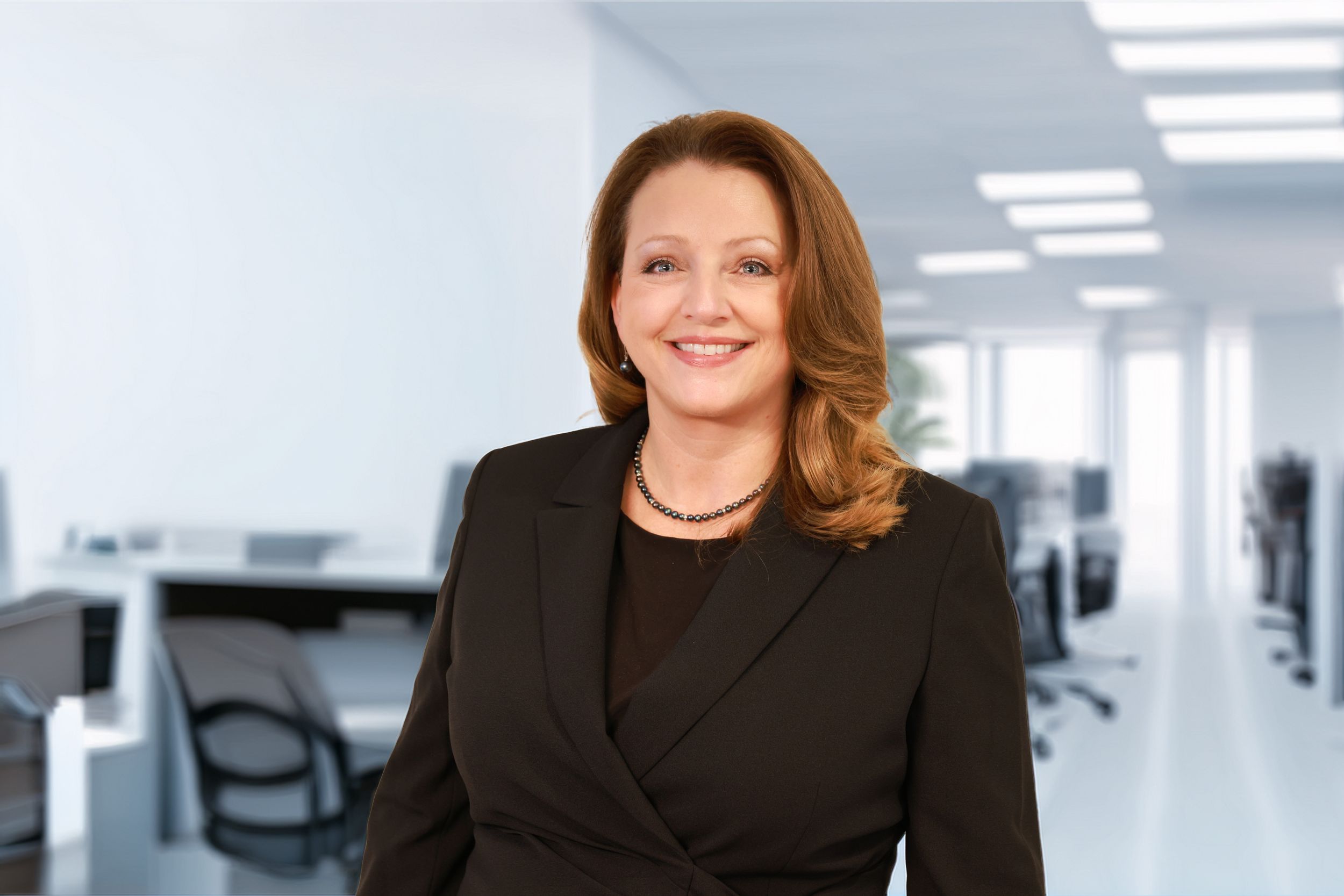 Professional headshot of someone in a black blazer smiling warmly against a bright office background.
