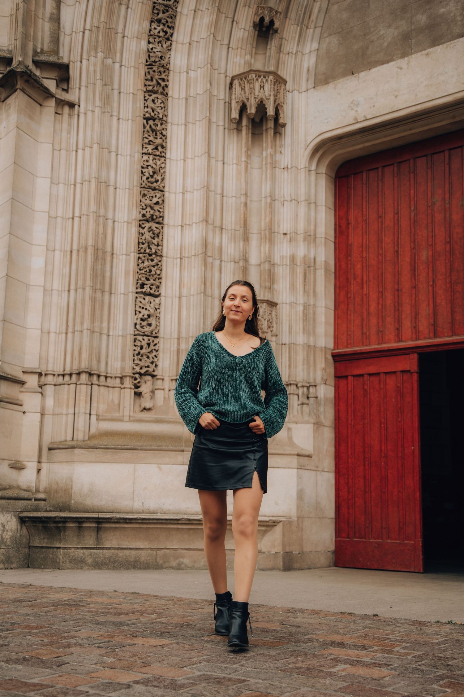 Woman in teal knit sweater and black mini skirt posing before Gothic cathedral entrance.