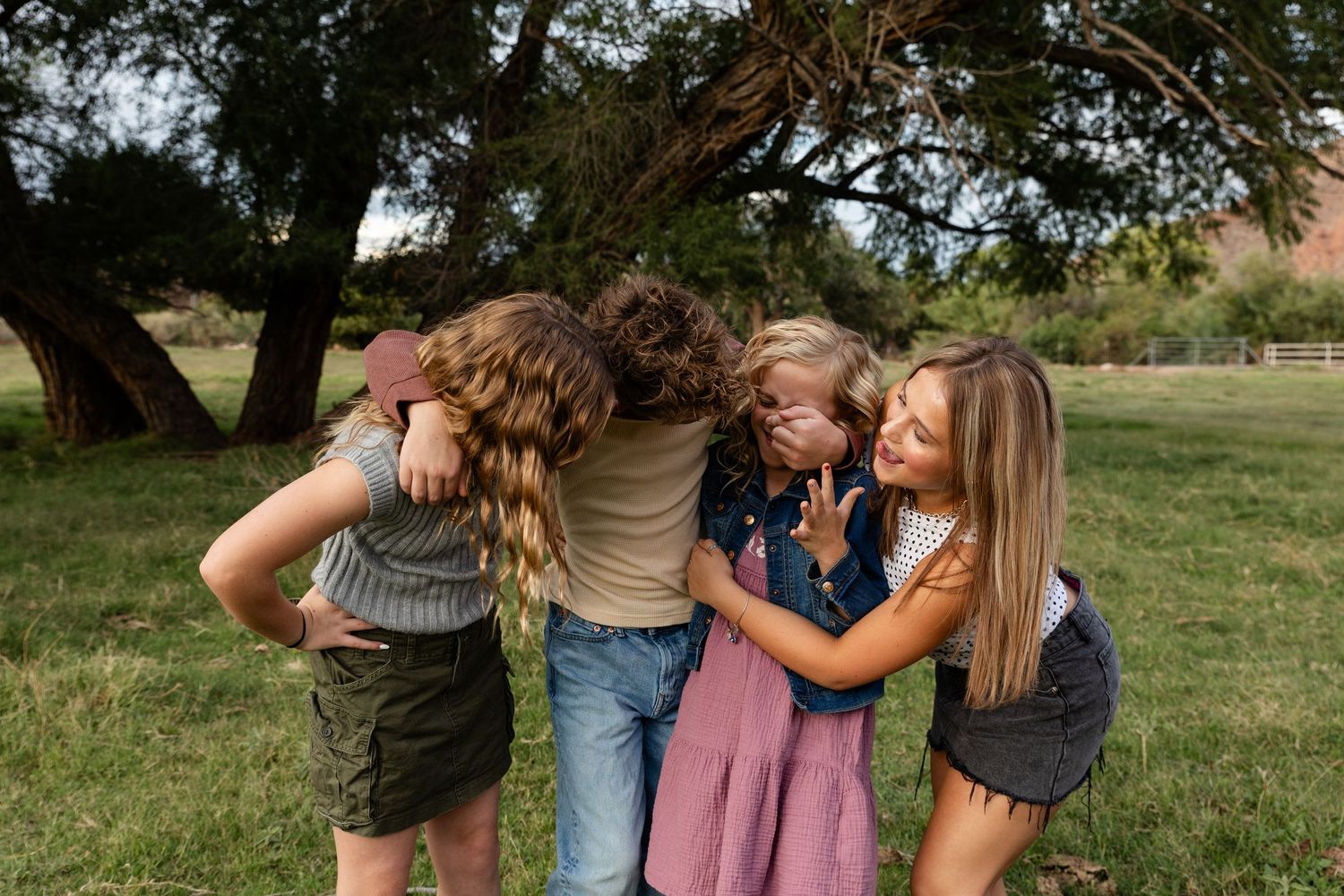 siblings laughing together in family photos St. George utah 4 kids 1 boy arms around each other tickling youngest sister. laughing