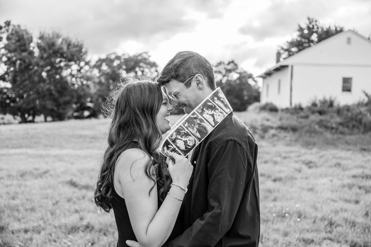 A romantic couple shares intimate moments in a series of black and white photographs taken in an outdoor field setting.