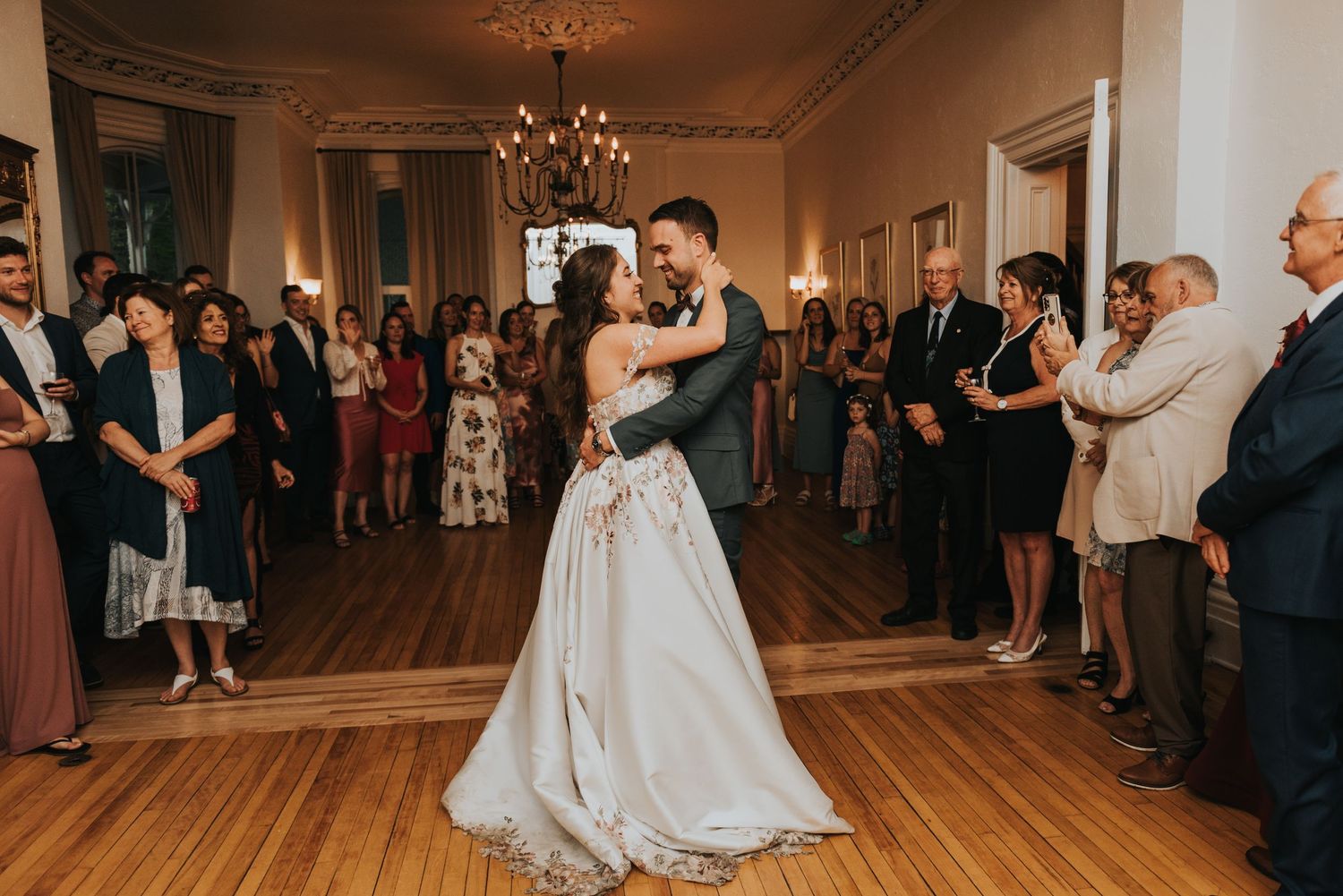 Wedding guests dance and celebrate on a hardwood floor in an elegant reception hall with warm lighting.