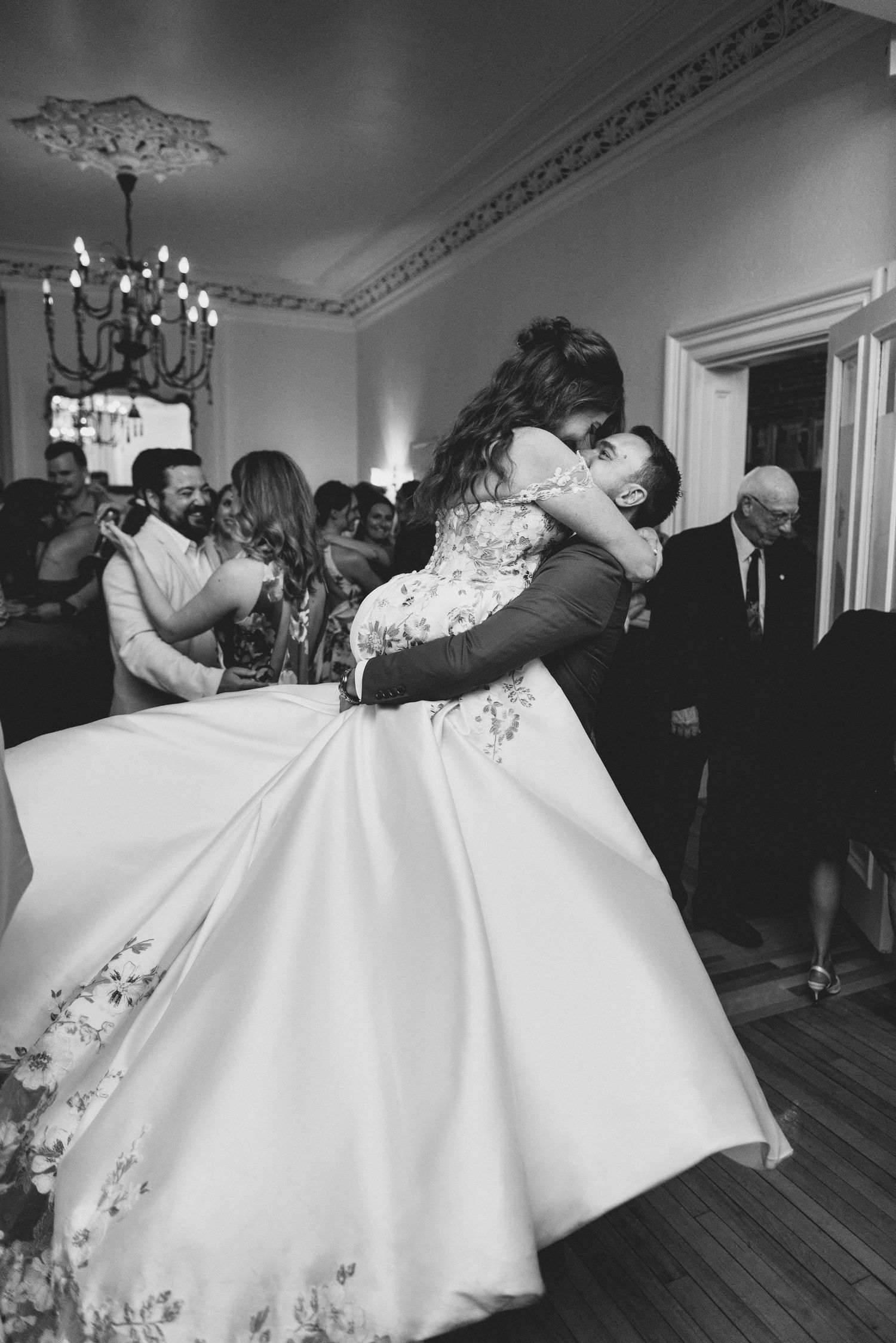 A couple performs a dramatic dance dip on a hardwood floor during a wedding reception celebration.