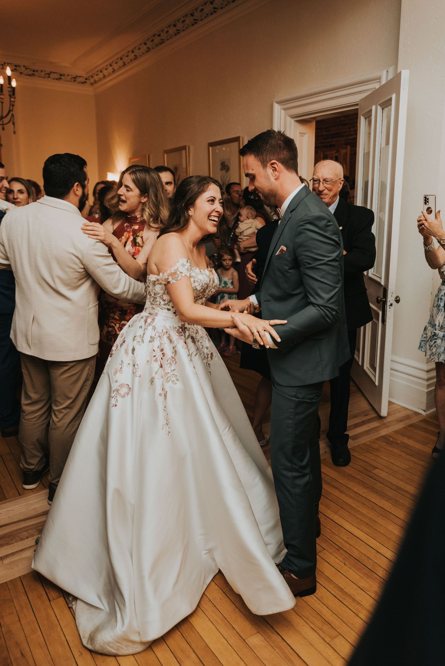 Couples dance together during a wedding reception in a classic ballroom with white trim and wooden floors.