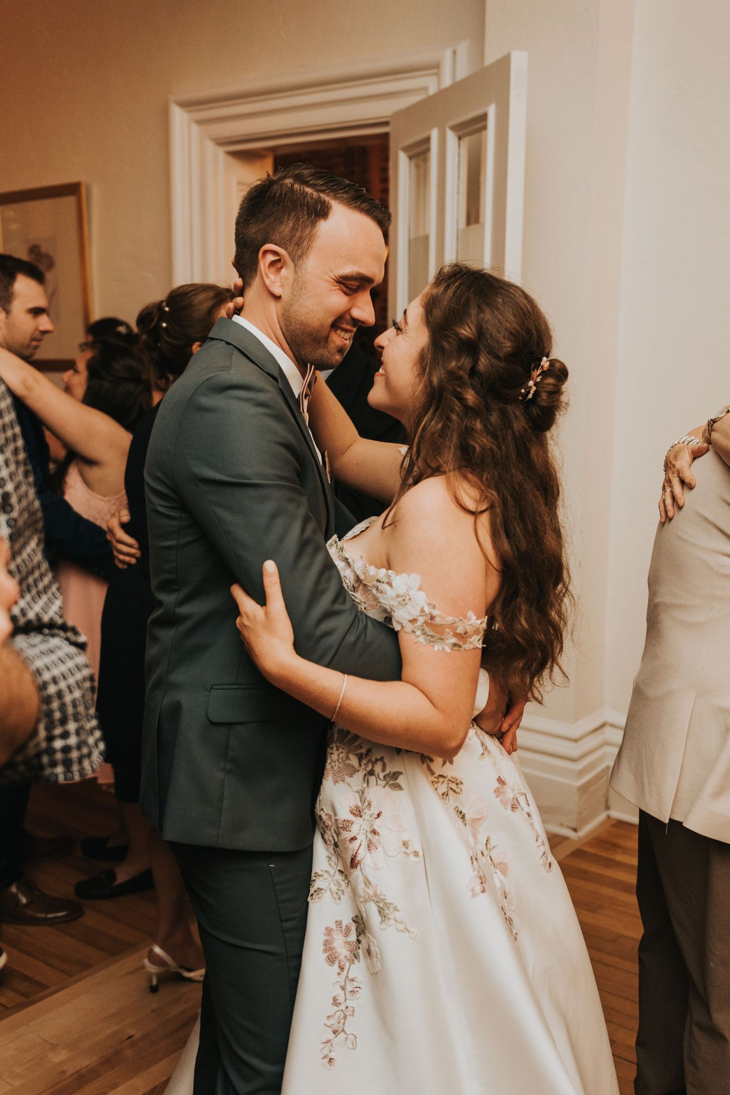 Wedding party members dance in pairs across a polished hardwood floor at an elegant indoor reception.