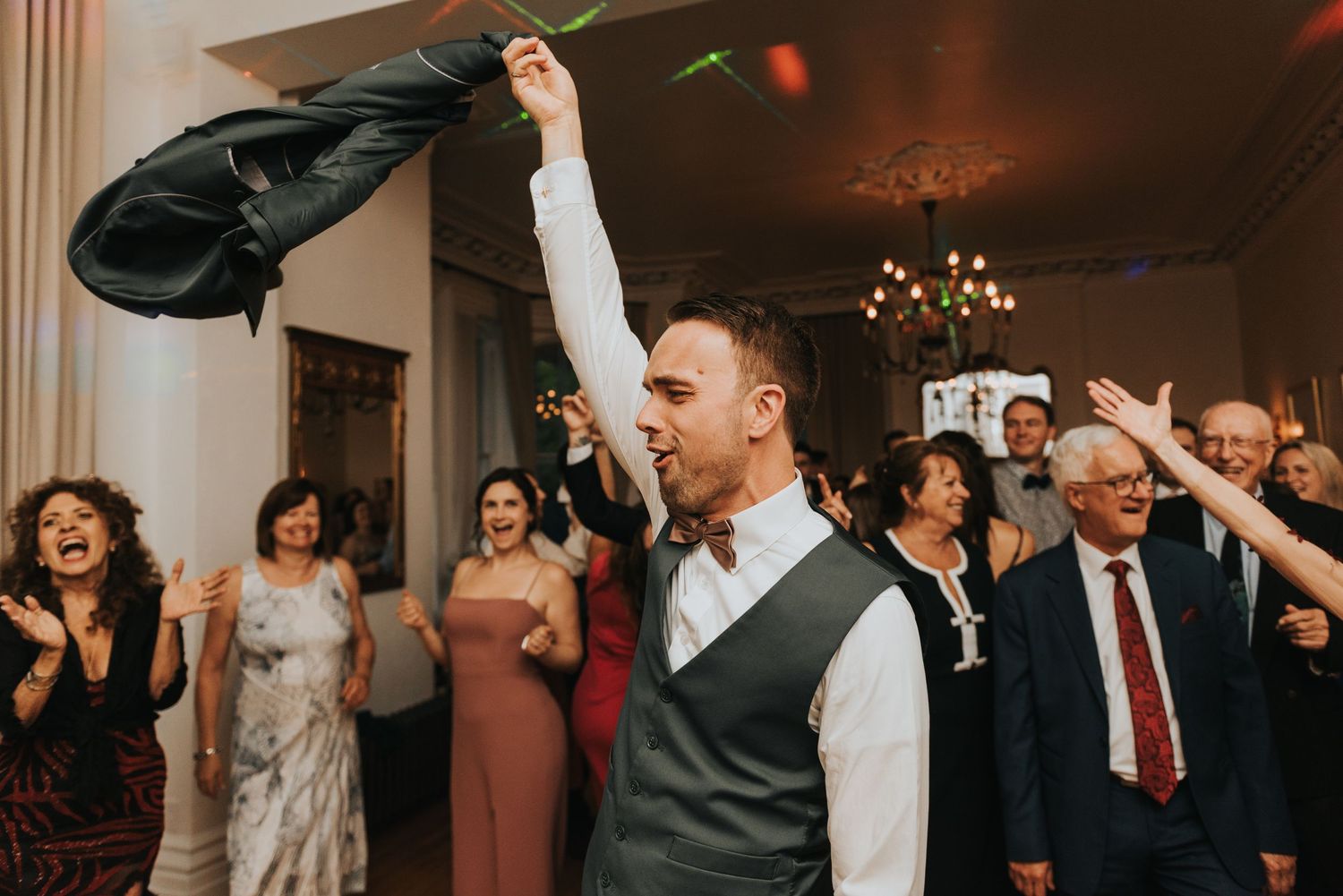 Guests enjoying themselves on a crowded dance floor during a wedding celebration with chandelier lighting.