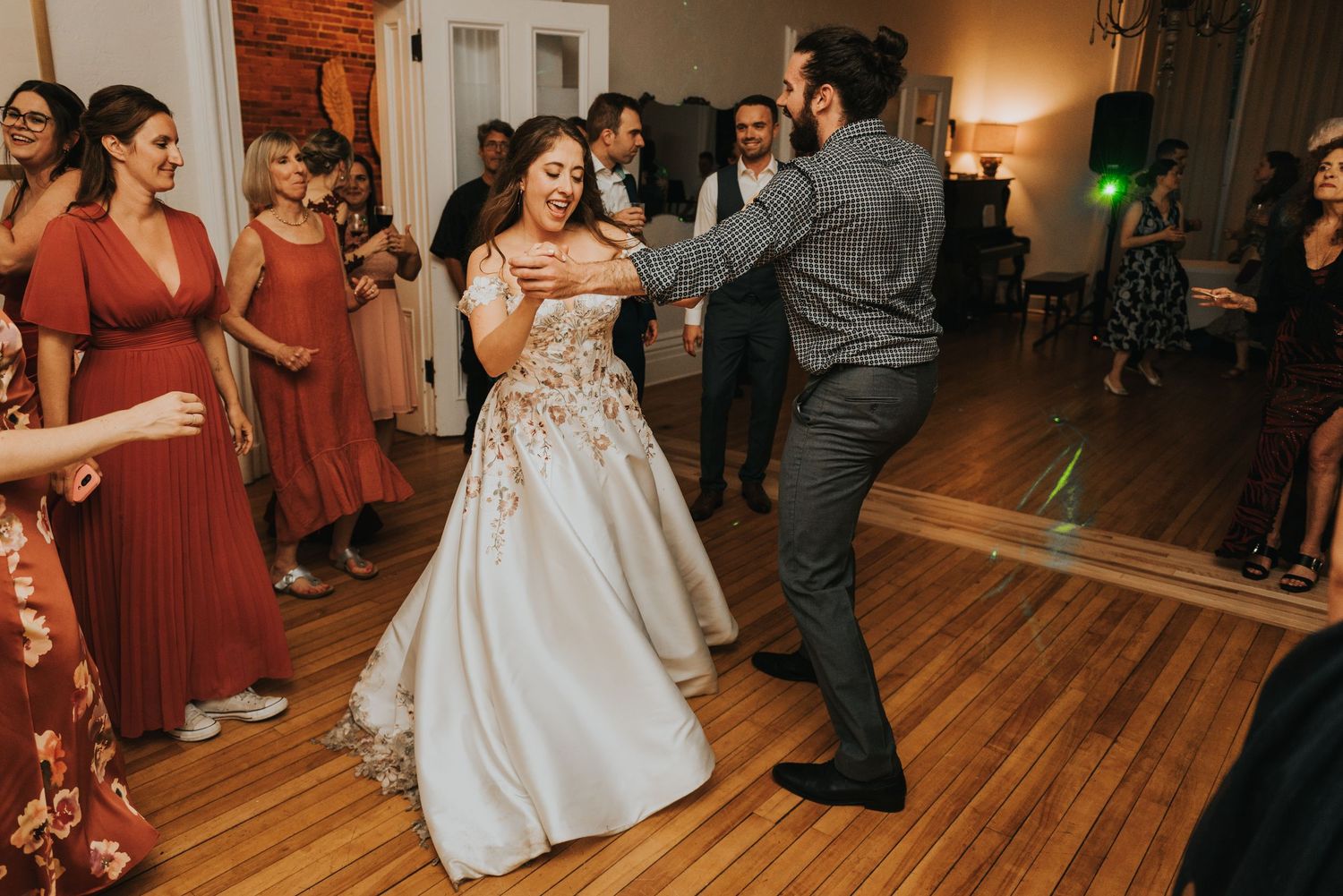 Wedding guests dance and celebrate on a wooden dance floor under elegant chandeliers.