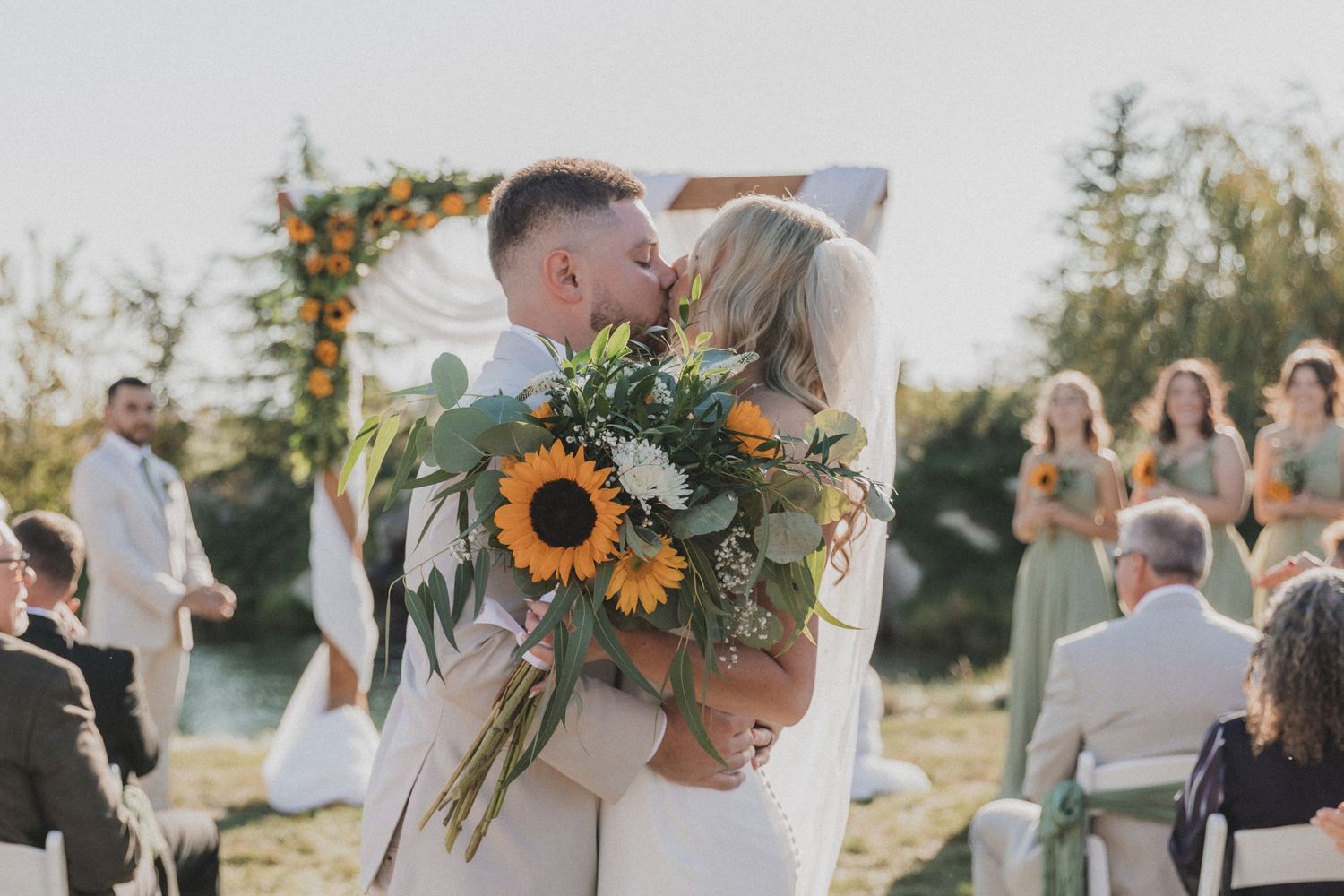 Wedding guests celebrate outdoors with bright sunflower bouquets and floral arrangements at sunset.