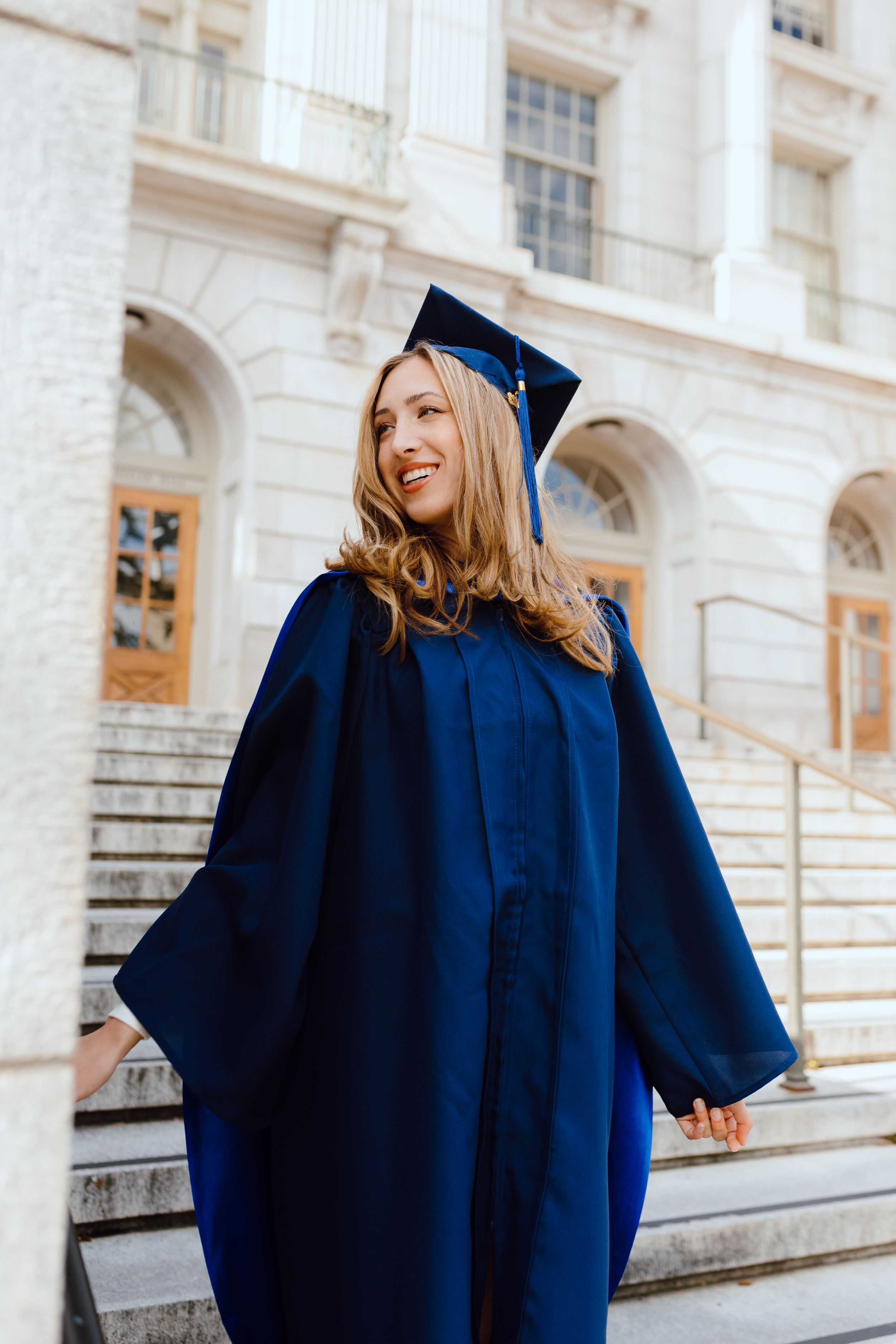 Graduate posing on campus steps wearing traditional graduation regalia. UC Berkeley graduation photoshoot.