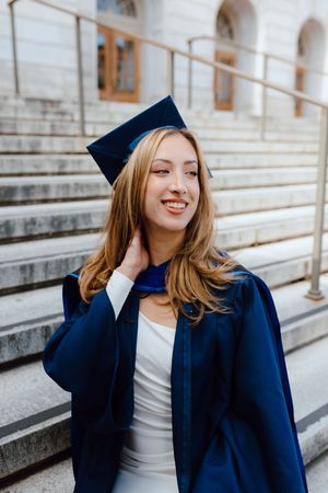 UC Berkeley graduate wearing a cap and gown poses outside one of the campus's beautiful buildings for her grad photoshoot.