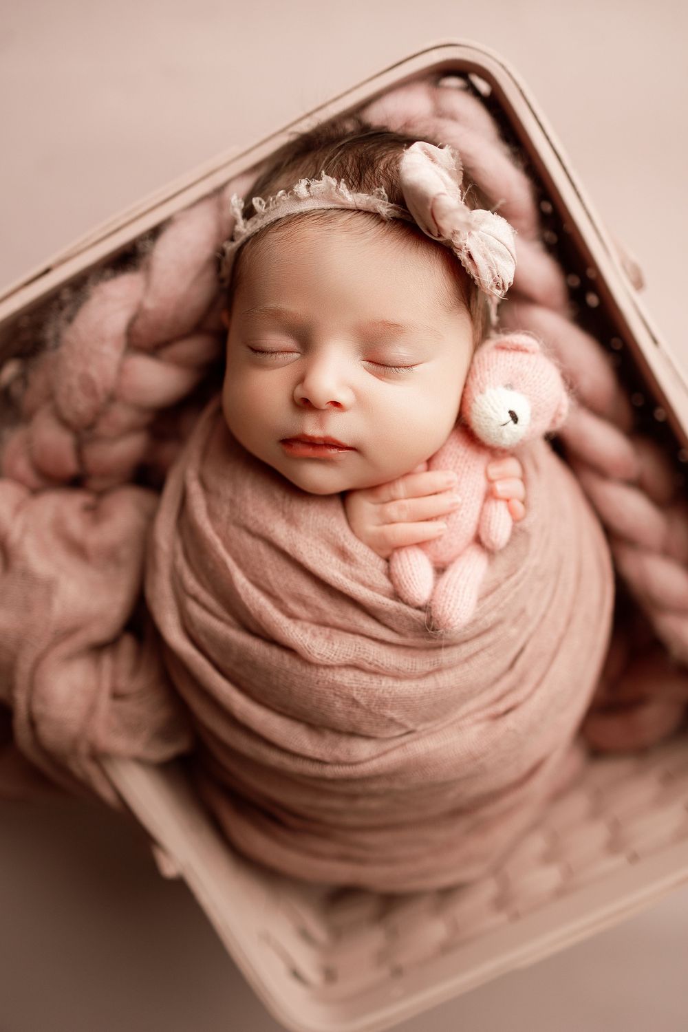 A peaceful newborn photography series showing a sleeping baby wrapped in soft pink fabric with a small plush bunny toy.