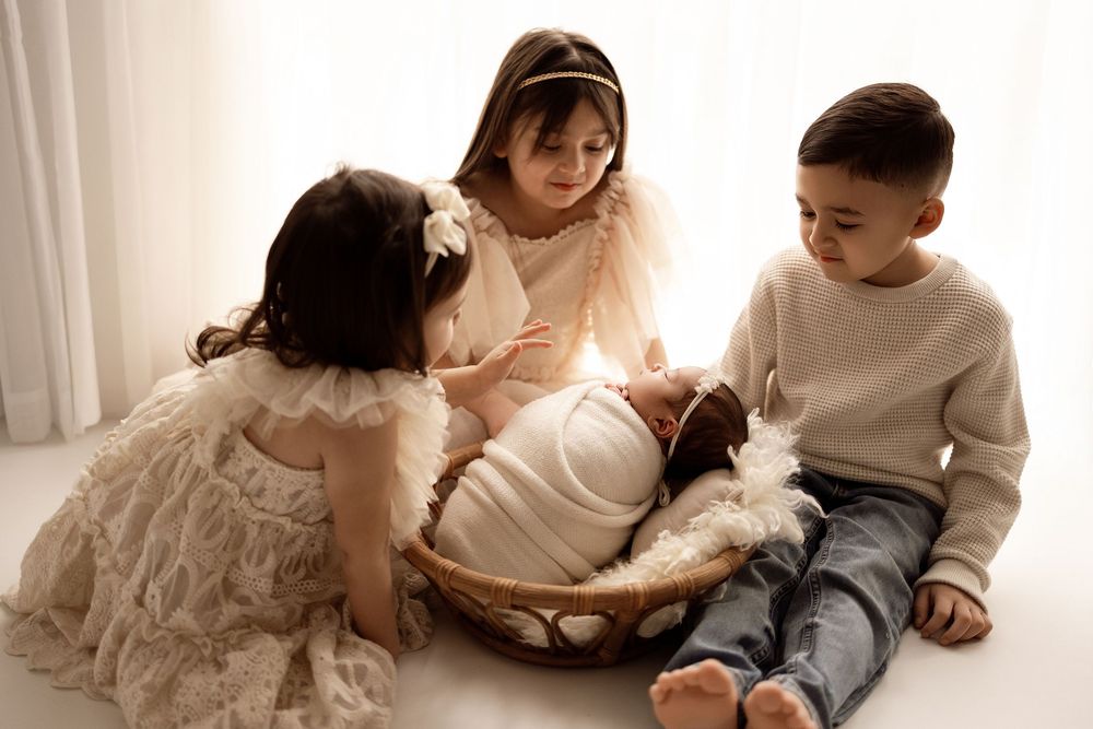 A family lying together on a white bed wearing casual clothes in a warm, intimate setting.
