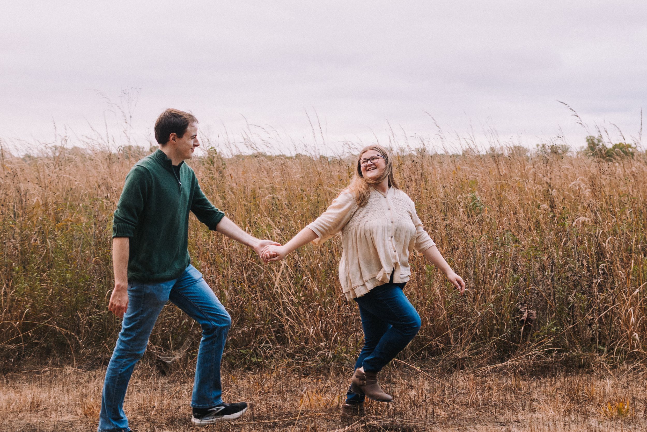 Playful couple dances in a golden field during sunset.