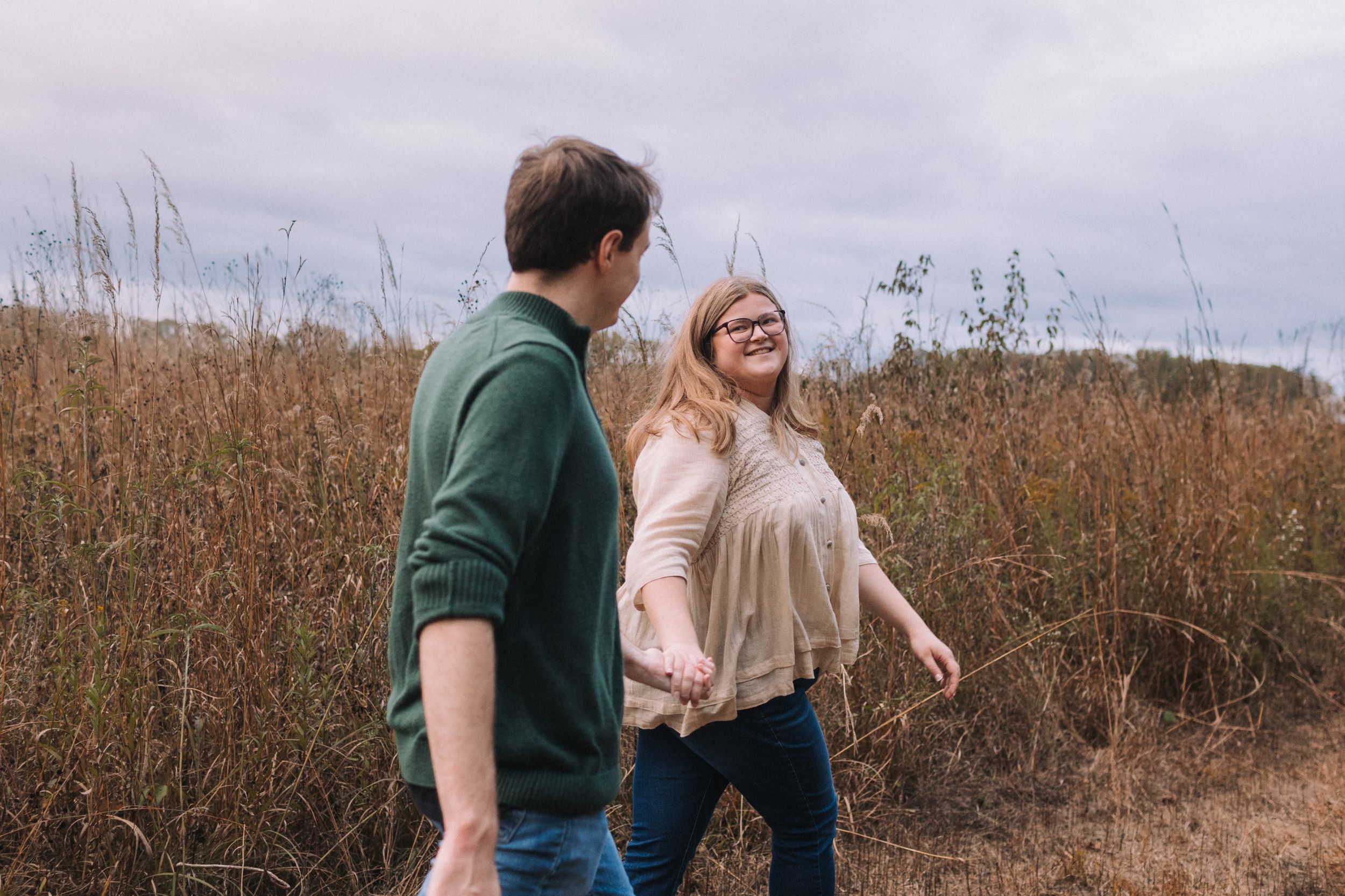 A couple laughs together in a natural setting with tall grass in the background.